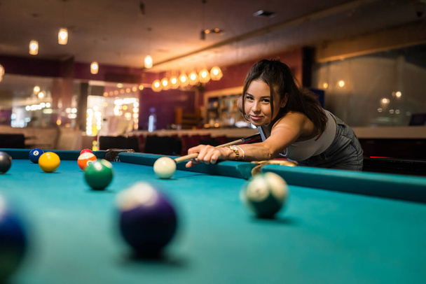 cheerful young woman playing billiard in pub. relax after hard day, lifestyle - Фото, изображение