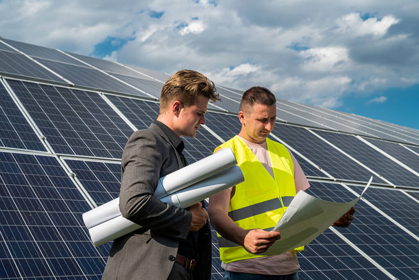 Project manager and worker discussing new solar panels installation with blueprints - Foto, Imagem