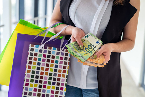 Молодая девушка с сумками для покупок считает евро деньги для следующей покупки, черная пятница. скидка - Фото, изображение