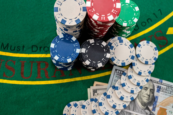 на игровом покерном столе находятся цветные фишки поверх друг друга и доллары рядом с ними. Концепция игры - Фото, изображение