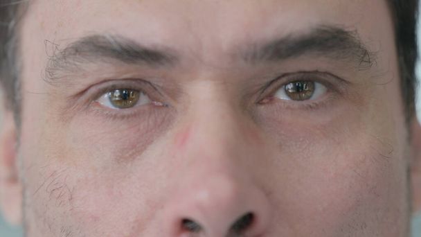 Закрыть мигающие глаза человека средних лет, смотрящего в камеру - Фото, изображение