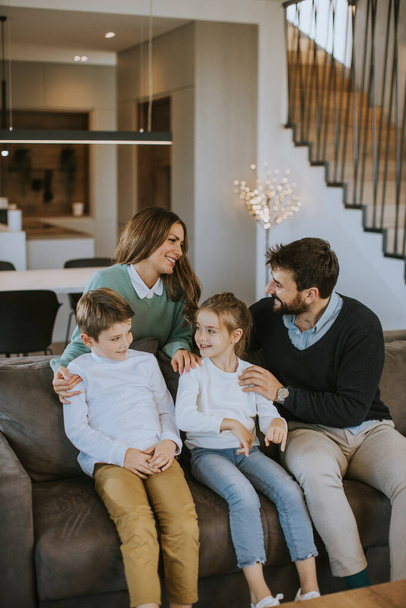 Glückliche junge Familie mit zwei Kindern genießt die gemeinsame Zeit auf der Couch im Wohnzimmer - Foto, Bild