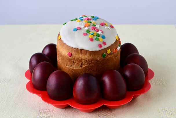 Traditional Easter cake with decorative glaze. Orthodox food after fasting on the Easter holiday. Red-painted chicken eggs on a stand on a light tablecloth - Photo, image