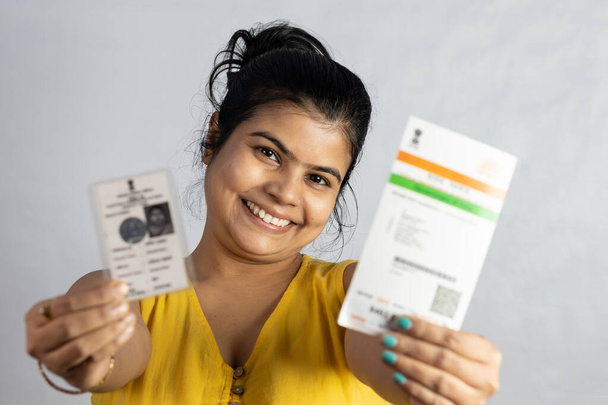 Una giovane donna indiana sorridente con carta Aadhaar e scheda elettorale in mano su sfondo bianco - Foto, immagini