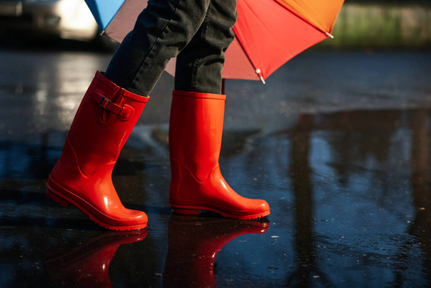 Woman with umbrella and red rubber boots walking in puddle, closeup. Rainy weather - Zdjęcie, obraz