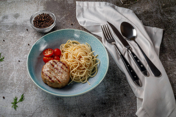 Spaghetti pasta with meat patty and fresh tomatoes on a blue plate against a gray stone table.  - Фото, зображення