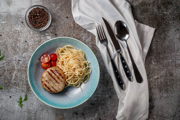 Pasta de espaguetis con empanada de carne y tomates frescos en un plato azul contra una mesa de piedra gris.  - Foto, Imagen