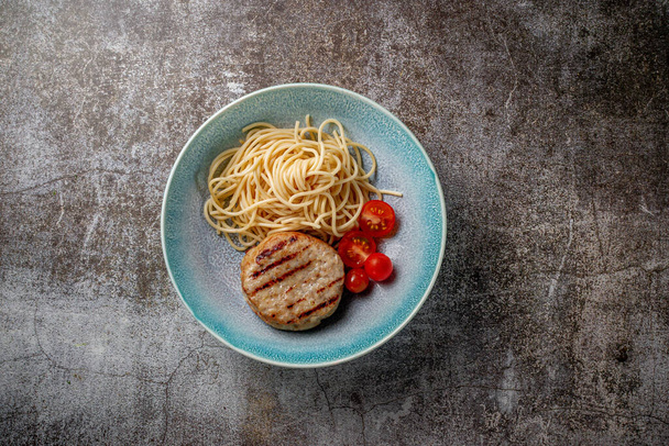 Spaghetti pasta with meat patty and fresh tomatoes on a blue plate against a gray stone table.  - Fotó, kép