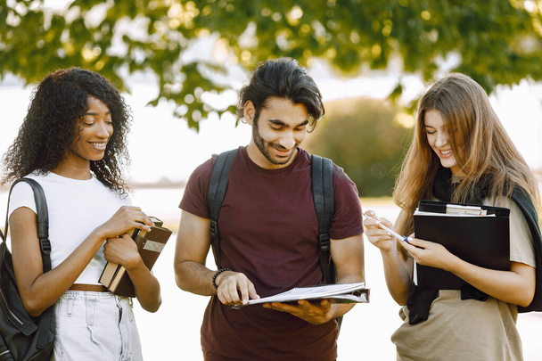 Three international students standing in a park and holding a books - Foto, Imagen