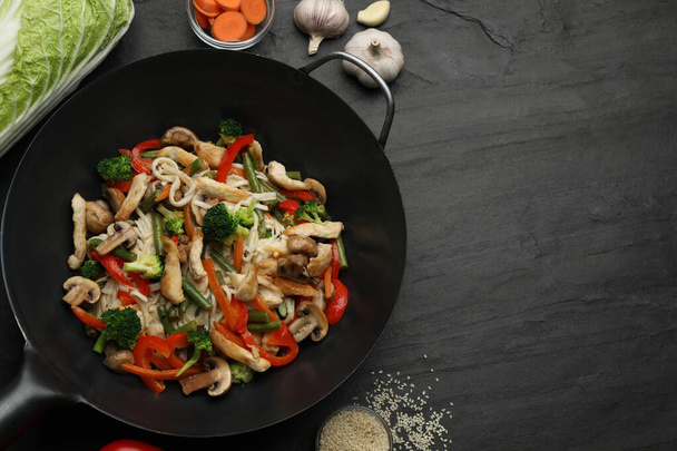 Stir fried noodles with mushrooms, chicken and vegetables in wok on black table, flat lay. Space for text - Φωτογραφία, εικόνα
