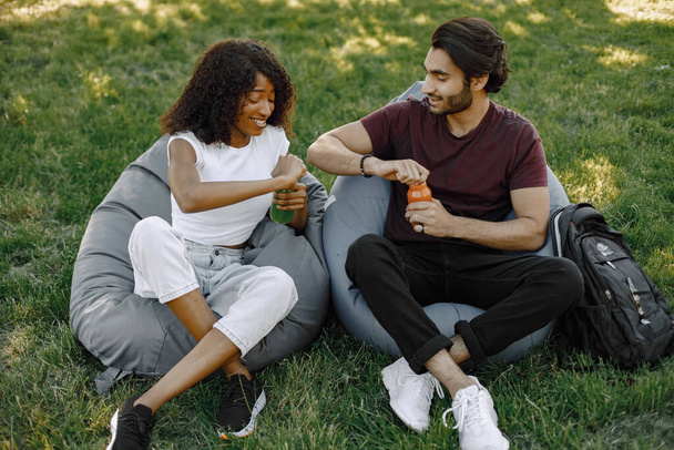 Indian boy and african girl talking sitting on the bean bag chairs in a park - Photo, Image