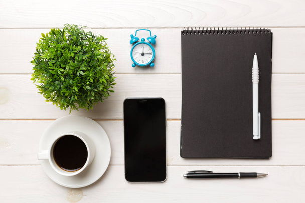 Moderne bureau tafel met notebook, smartphone en andere benodigdheden met kopje koffie. Blanco notitieboek pagina voor u ontwerp. Bovenaanzicht, vlak lay. - Foto, afbeelding