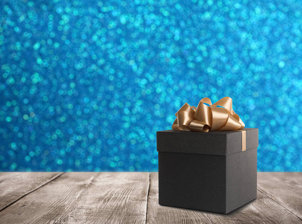 Beautiful gift box on wooden table against shiny light blue background, bokeh effect. Space for text - Фото, изображение