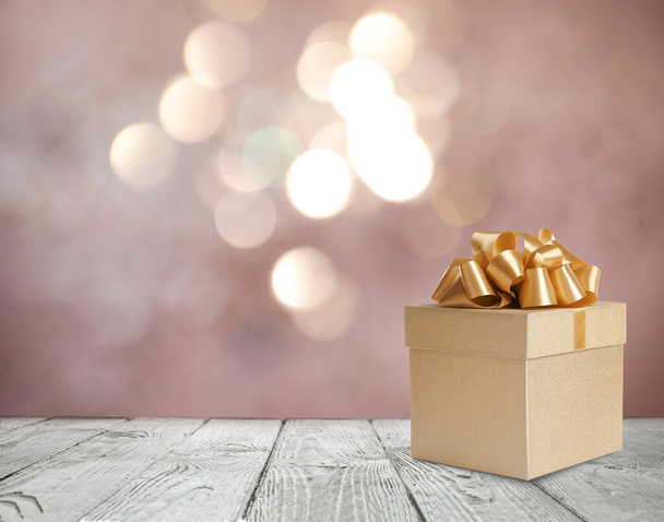 Beautiful gift box on white wooden table against blurred festive lights, bokeh effect. Space for text - Фото, изображение