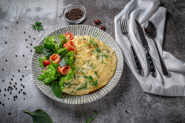 Omelet with salmon, fresh herbs and tomatoes in a blue plate with spices against a gray stone table - Fotografie, Obrázek