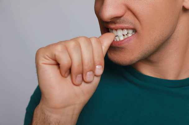 Man biting his nails on grey background, closeup. Bad habit - Fotografie, Obrázek