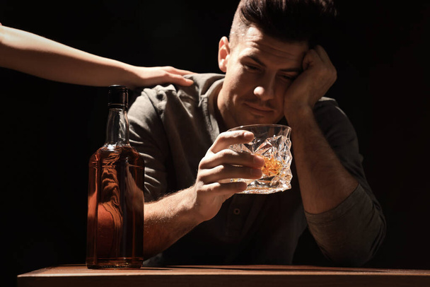 Addicted man at wooden table against black background, focus on glass of alcoholic drink - Foto, Bild