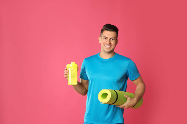Handsome man with yoga mat and shaker on pink background - Фото, изображение