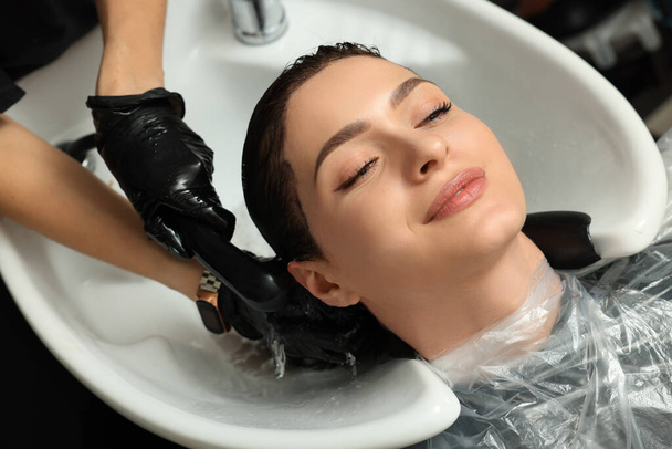 Hairdresser rinsing out dye from woman's hair in beauty salon - Foto, Imagen