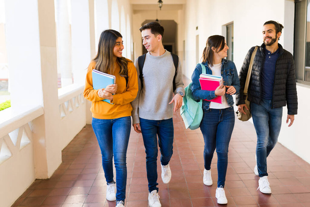 Iloiset opiskelijat kävelevät käytävällä puhuessaan läksyistä luokan jälkeen. - Valokuva, kuva