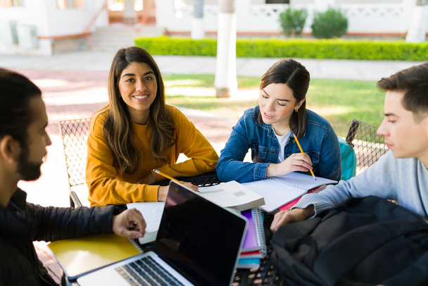 Grupo de estudio diverso. Estudiante latina mirando a la cámara mientras hace los deberes con amigos universitarios - Foto, imagen