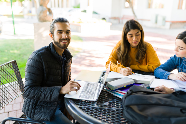 Retrato de un estudiante hispano haciendo contacto visual mientras estudia e investiga en línea con amigos universitarios - Foto, imagen