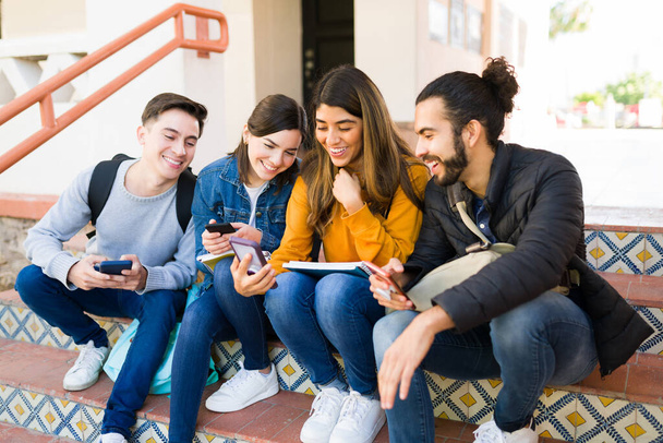 Cheerful young woman showing her college friends an online picture on her smartphone and laughing  - Photo, Image