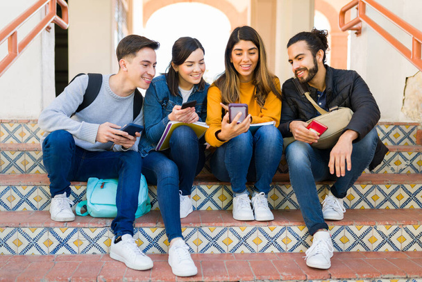 Aantrekkelijke multiraciale college vrienden sms 'en en het gebruik van smartphones tijdens het zitten op de trap van de universiteit  - Foto, afbeelding