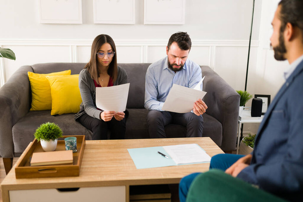 Hermosa pareja de 30 años leyendo un contrato de arrendamiento para alquilar una casa nueva con un agente de bienes raíces  - Foto, imagen