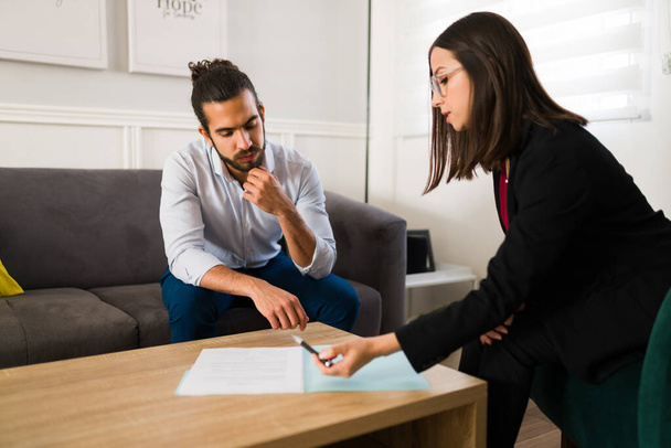 Professional finance advisor explaining a new business contract or life insurance to an attractive young man at his home - Photo, Image