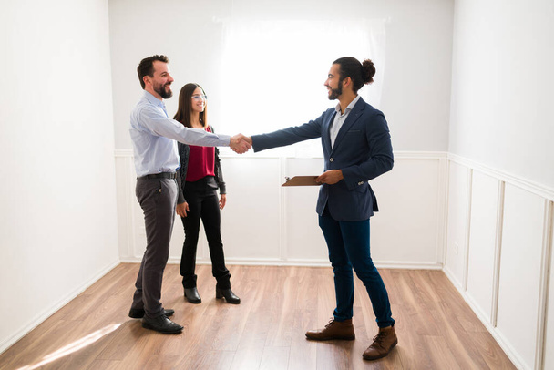 This is the new home for you. Hispanic realtor shaking hands with new clients doing a property tour in a new home  - Zdjęcie, obraz