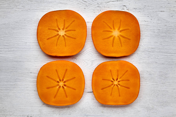 Ripe orange persimmon sliced sliced lined on a white wooden table - Φωτογραφία, εικόνα