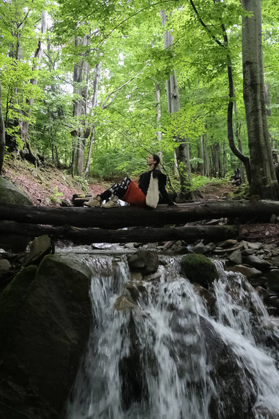 una donna siede su un tronco vicino a un ruscello nella foresta - Foto, immagini