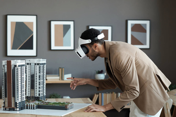 Young biracial businessman bending over table and pointing at house layout - Foto, afbeelding