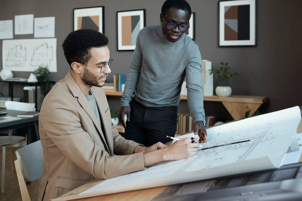 Two young intercultural businessmen discussing sketch of architecture on blueprint - Fotó, kép