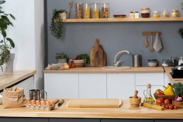 Keukentafel met houten plank, keukengerei, groenten en ingrediënten voor deeg - Foto, afbeelding