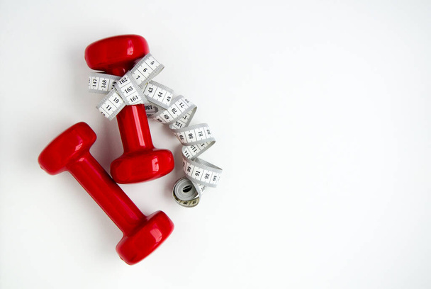 Two red dumbbells, white measuring tape on white background with copy space. Concept of Valentines day, healthy lifestyle, giving gifts, love of sports, shopping - Foto, immagini
