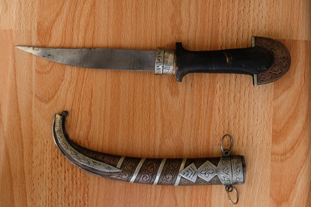 Old decorative knife dagger and scabbard on a wooden table. Hunting knife. Top view. - Valokuva, kuva