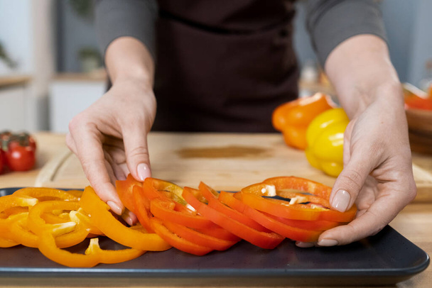 Hands of young female putting fresh chopped pepper on tray - Foto, imagen