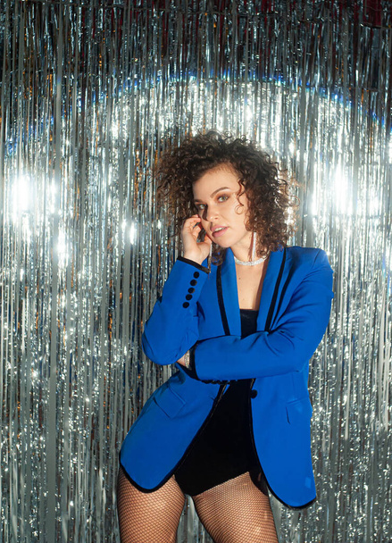  curly haired woman in blue jacket posing on sparkling disco background - Fotografie, Obrázek
