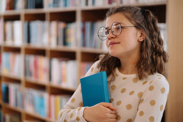 Beautiful girl is holding a book while standing on the floor among books in the bookshop - Foto, Imagen