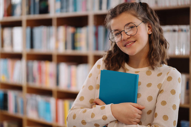 Όμορφη κοπέλα κρατά ένα βιβλίο ενώ στέκεται στο πάτωμα ανάμεσα στα βιβλία στο βιβλιοπωλείο - Φωτογραφία, εικόνα