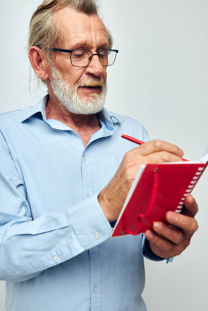 Portrait of happy senior man writes down emotions in a notebook light background - Foto, afbeelding