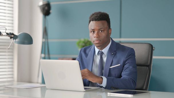 Afrikkalainen liikemies Tarkasteltaessa kameraa, kun käytät kannettavaa toimistossa - Valokuva, kuva