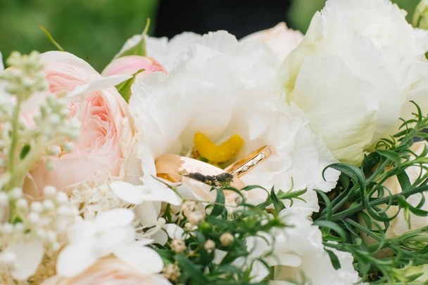 Goldene Eheringe und ein wunderschöner Hochzeitsstrauß aus Rosen und Eustoma im Hintergrund in Nahaufnahme. Details und Hochzeitstraditionen. - Foto, Bild