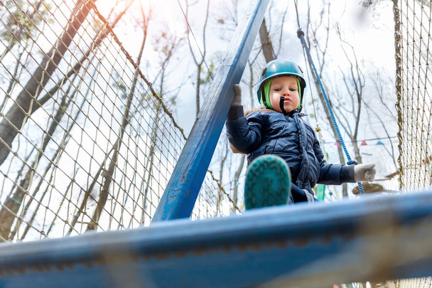 Нижній вид POV сміливий сміливий маленький малюк дитячий хлопчик носити шолом безпеки обладнання, насолоджуватися проходженням перешкод курс лісових мотузок пригод парк в холодний зимовий день. Активний відпочинок на вулиці розважальний табір
 - Фото, зображення