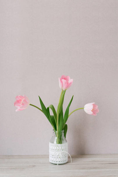  ramo de tres tulipanes rosados se encuentra en un jarrón de vidrio con encaje. El concepto del festival de primavera - Foto, imagen