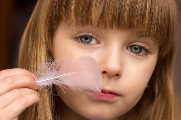 Portrait of a blurred little girl close-up and a feather of a bird in her hands stroking her cheek, gentle touch of smooth soft skin, selective focus - Foto, afbeelding