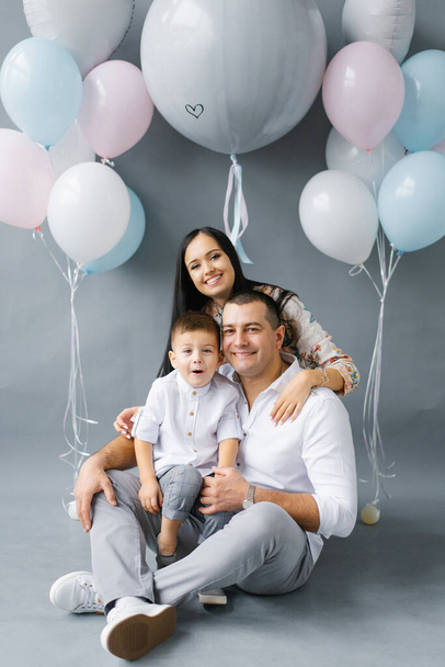 A young stylish family waiting for their second child against the background of a pop ball to determine the sex of the unborn child. Parents with their eldest son on a gray background. Gender reveal party - Valokuva, kuva