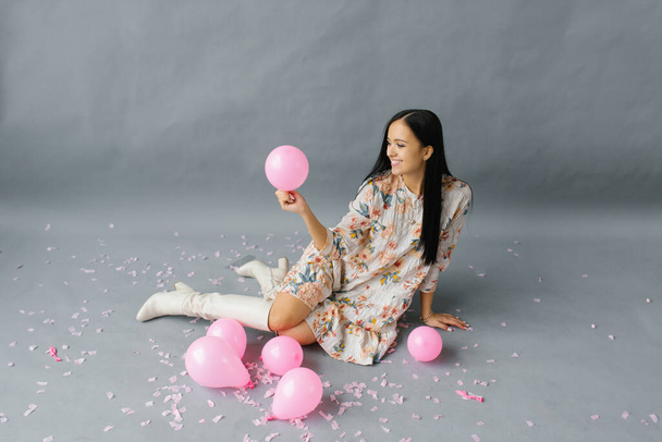 Zdjęcie wesołej kobiety, która czuje się bardzo szczęśliwa, trzymając różowy balon i śmiejąc się, pozując w pobliżu balonów - Zdjęcie, obraz